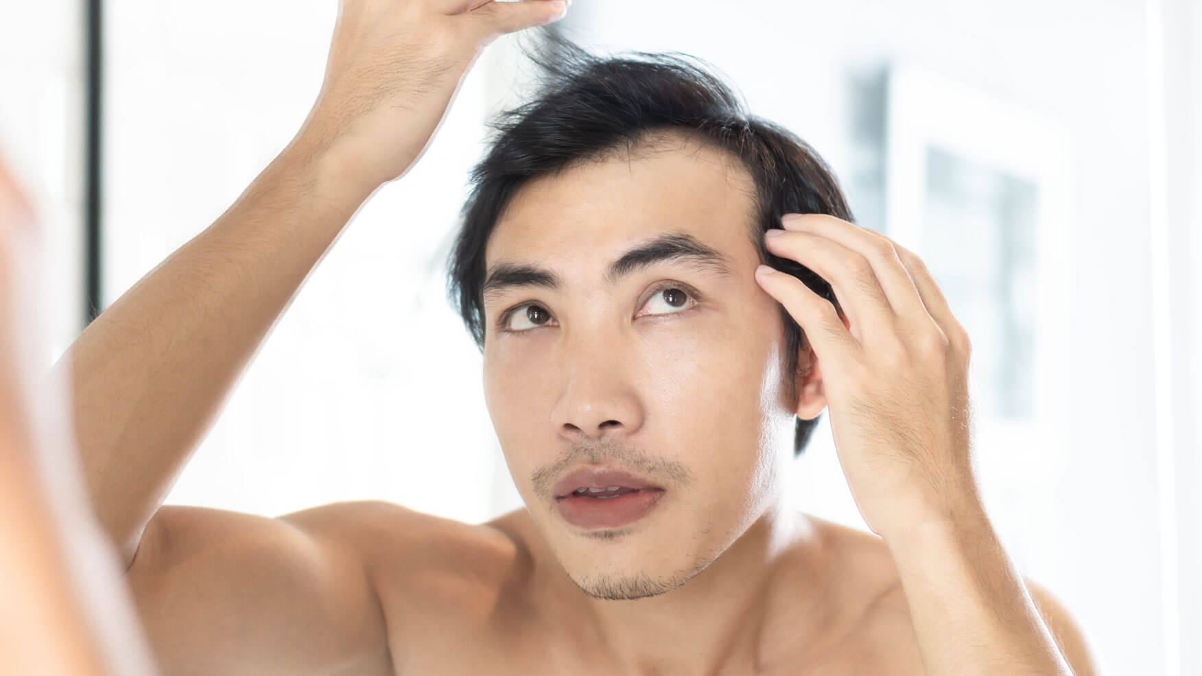 A topless man examining his hair in the mirror