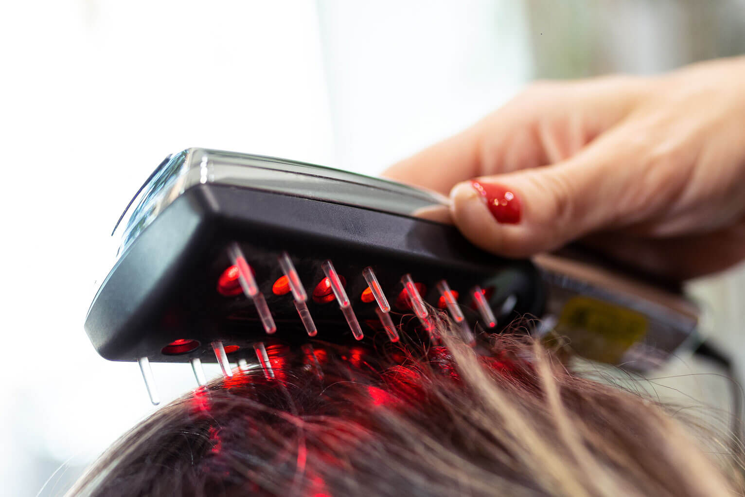 A woman uses a low level laser therapy comb on a customer's hair