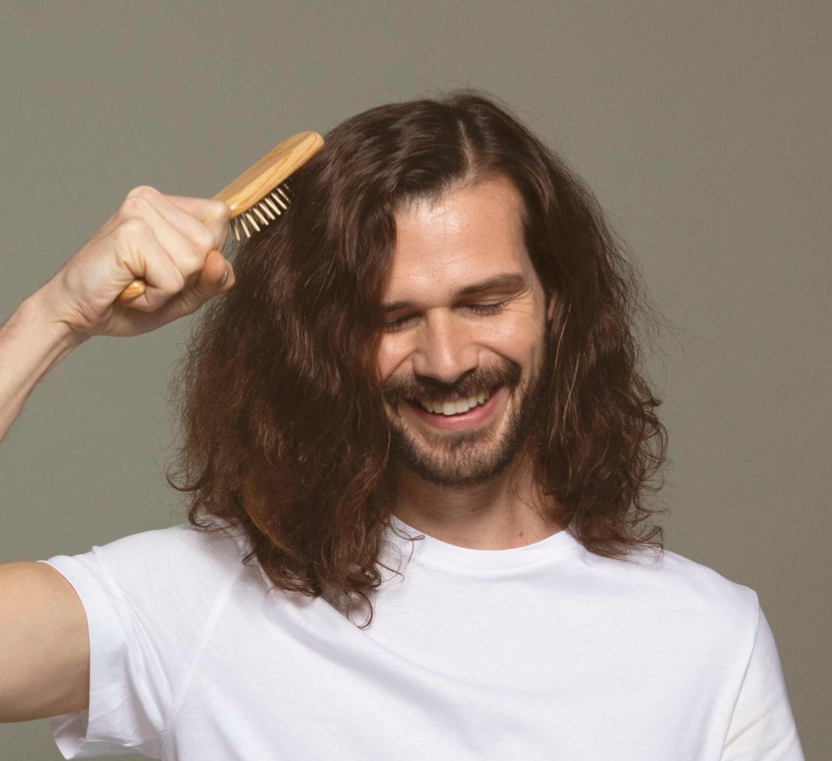 A man in a white t-shirt brushing his shoulder-length, wavy hair