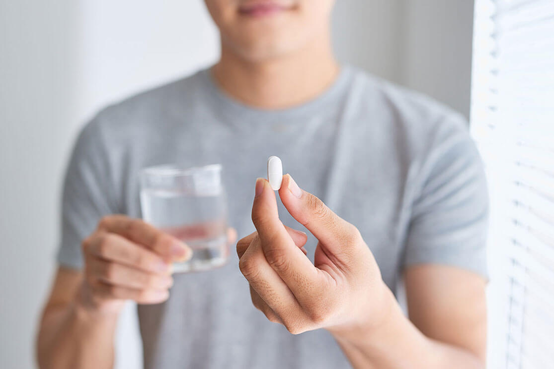 Close-up of the torso of a man holding  a supplement and water in his hands