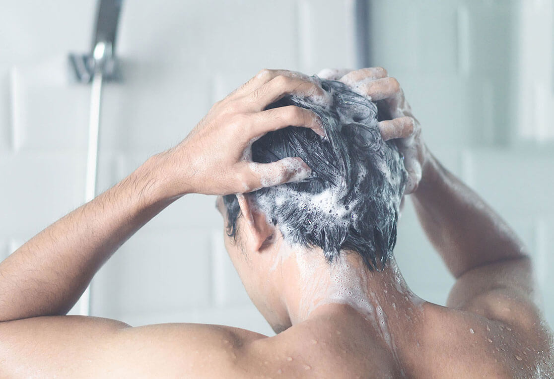 A man facing backwards, shampooing his hair in the shower