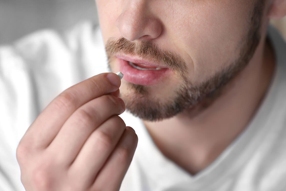 Close-up of a man holding a pill to his mouth