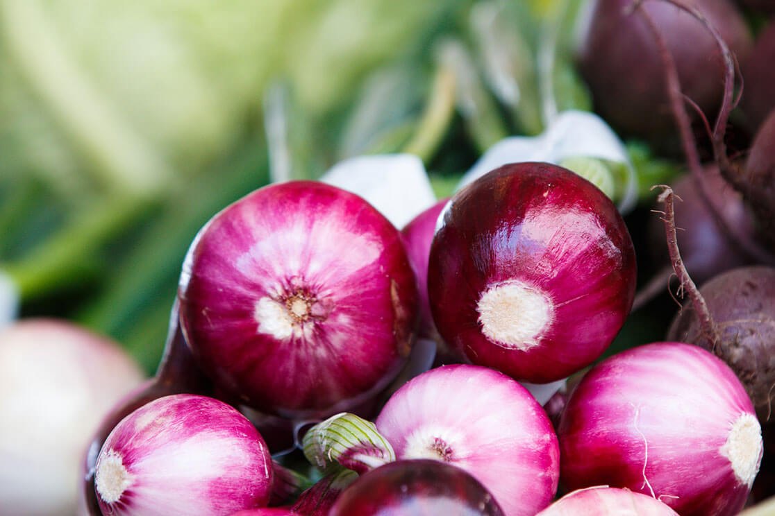 A pile of red onions against an out-of-focus green background