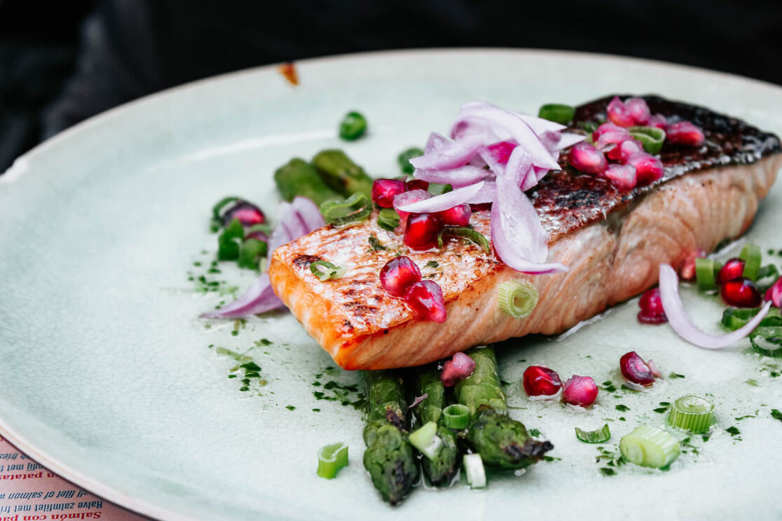 A plate, with broiled salmon and asparagus, garnished with pickled onion, chopped scallions, and pomegranate.